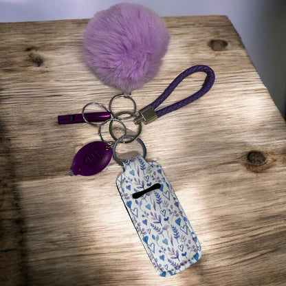 Keychain with purple pom-pom and floral tag on a wooden surface
