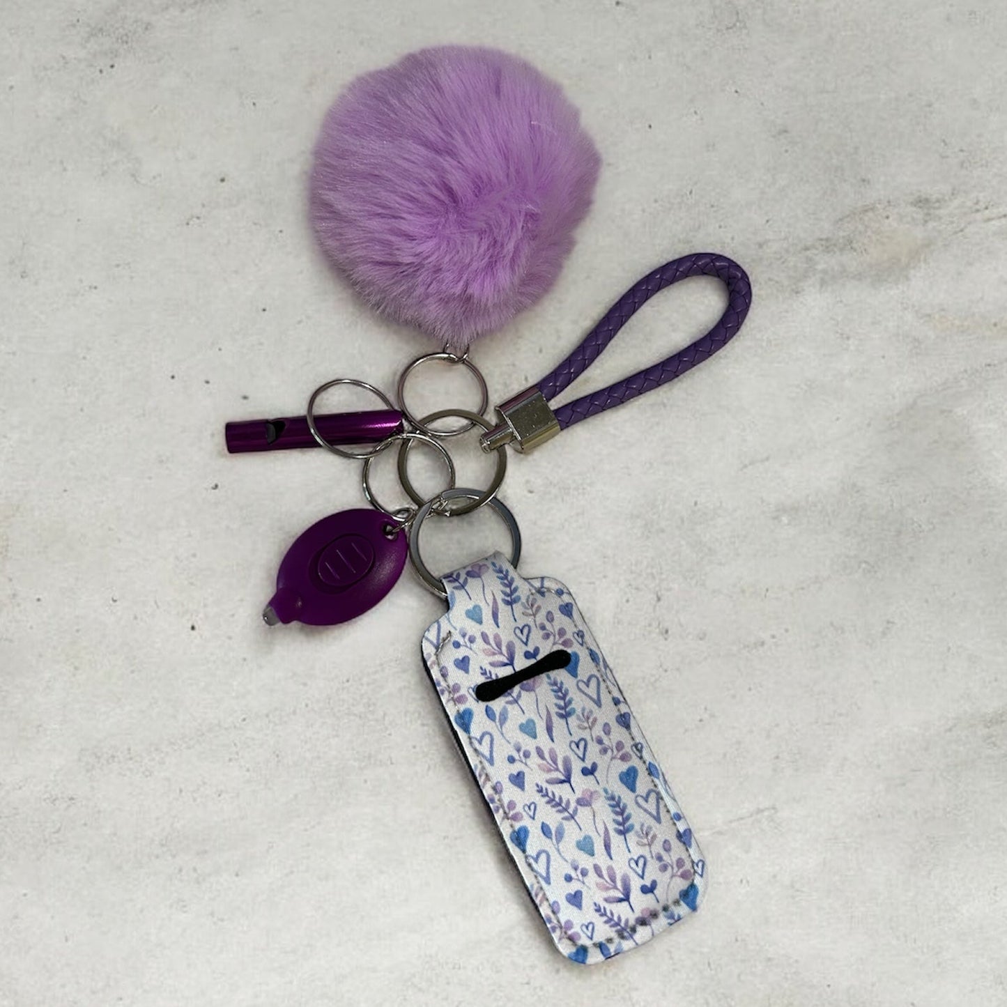 Keychain with purple pom-pom and floral tag on a light gray background